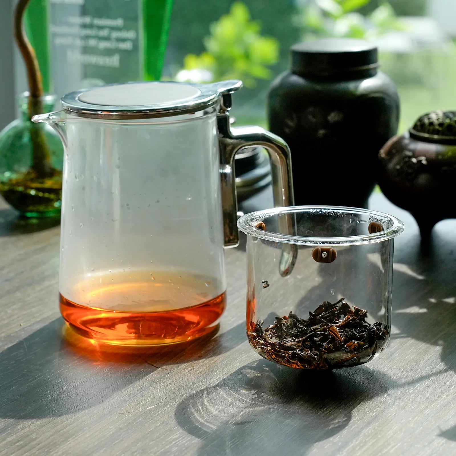 Glass teapot with tea and a glass cup with tea leaves on a wooden surface.