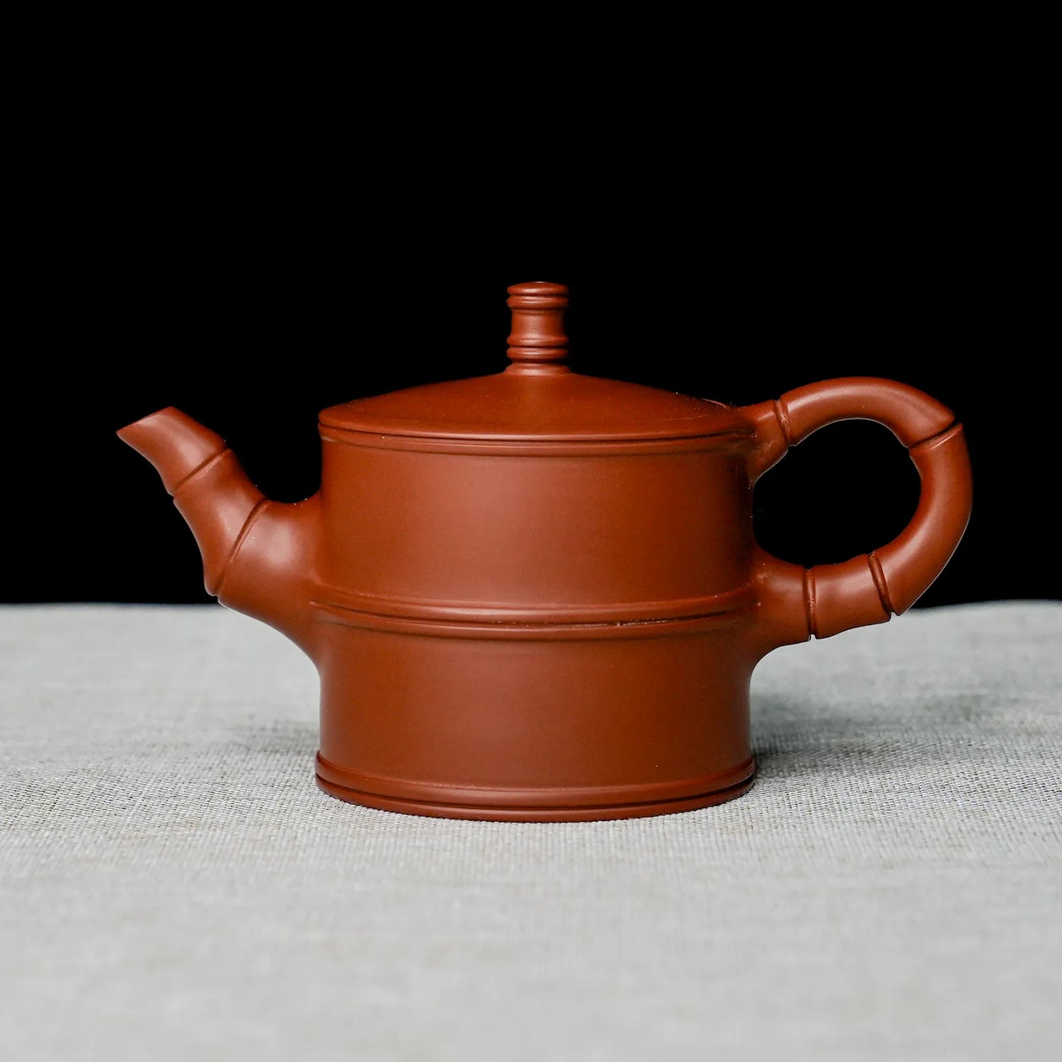 Red clay teapot on a textured surface with a black background