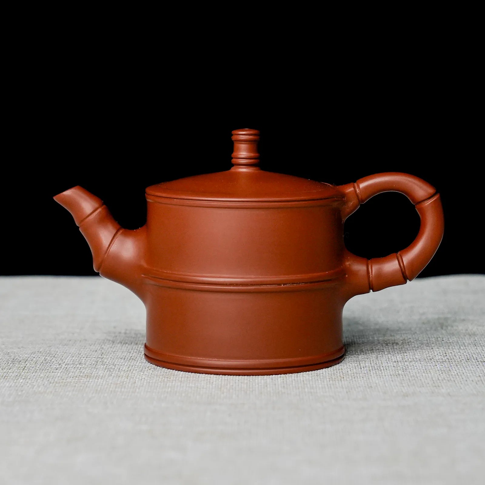Red clay teapot on a textured surface with a black background