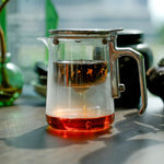 Clear glass teapot with a metal handle and lid on a wooden surface.