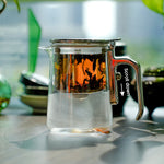 Clear glass teapot with a metal handle on a blurred background