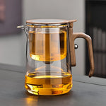 Clear glass teapot with wooden handle filled with tea on a wooden surface.