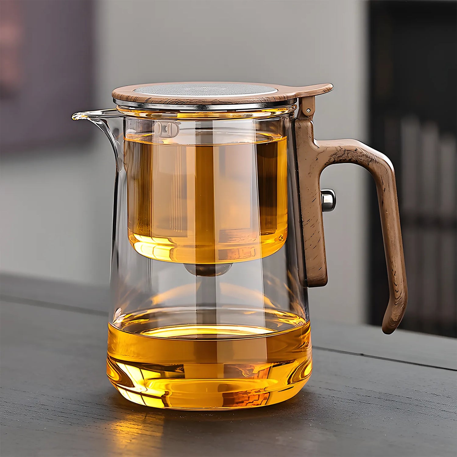 Clear glass teapot with wooden handle filled with tea on a wooden surface.