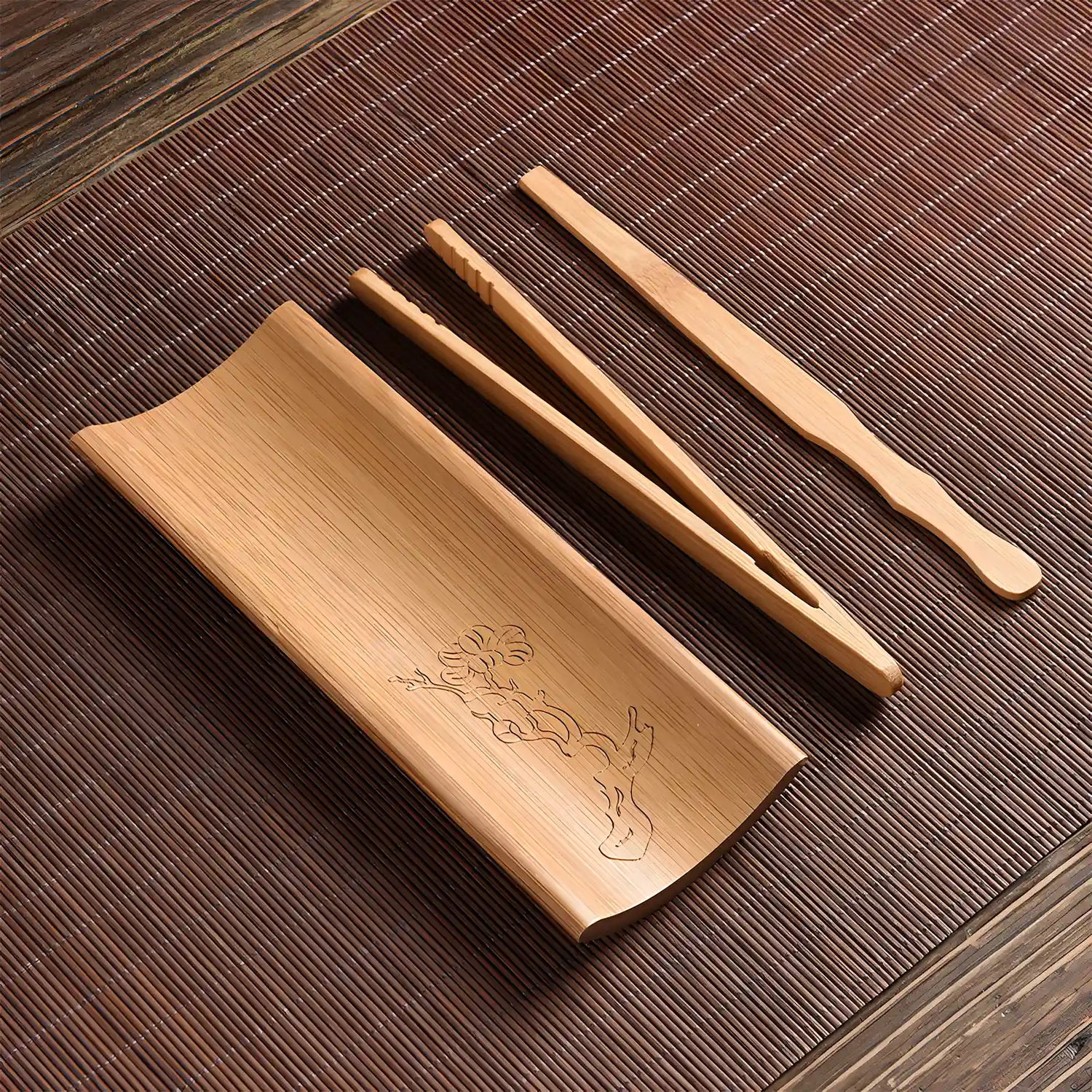 Bamboo tea set with a tray, tongs, and a spoon on a wooden surface.