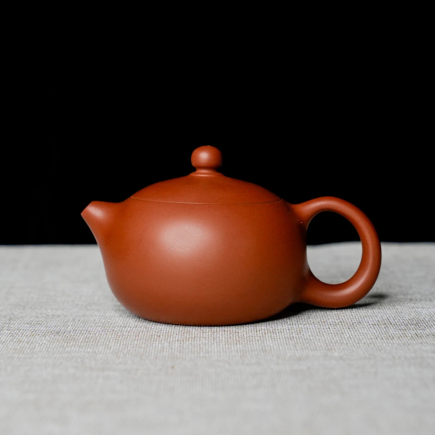 Red clay teapot on a textured surface with a black background