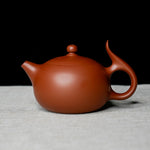 Red clay teapot on a textured surface with a black background