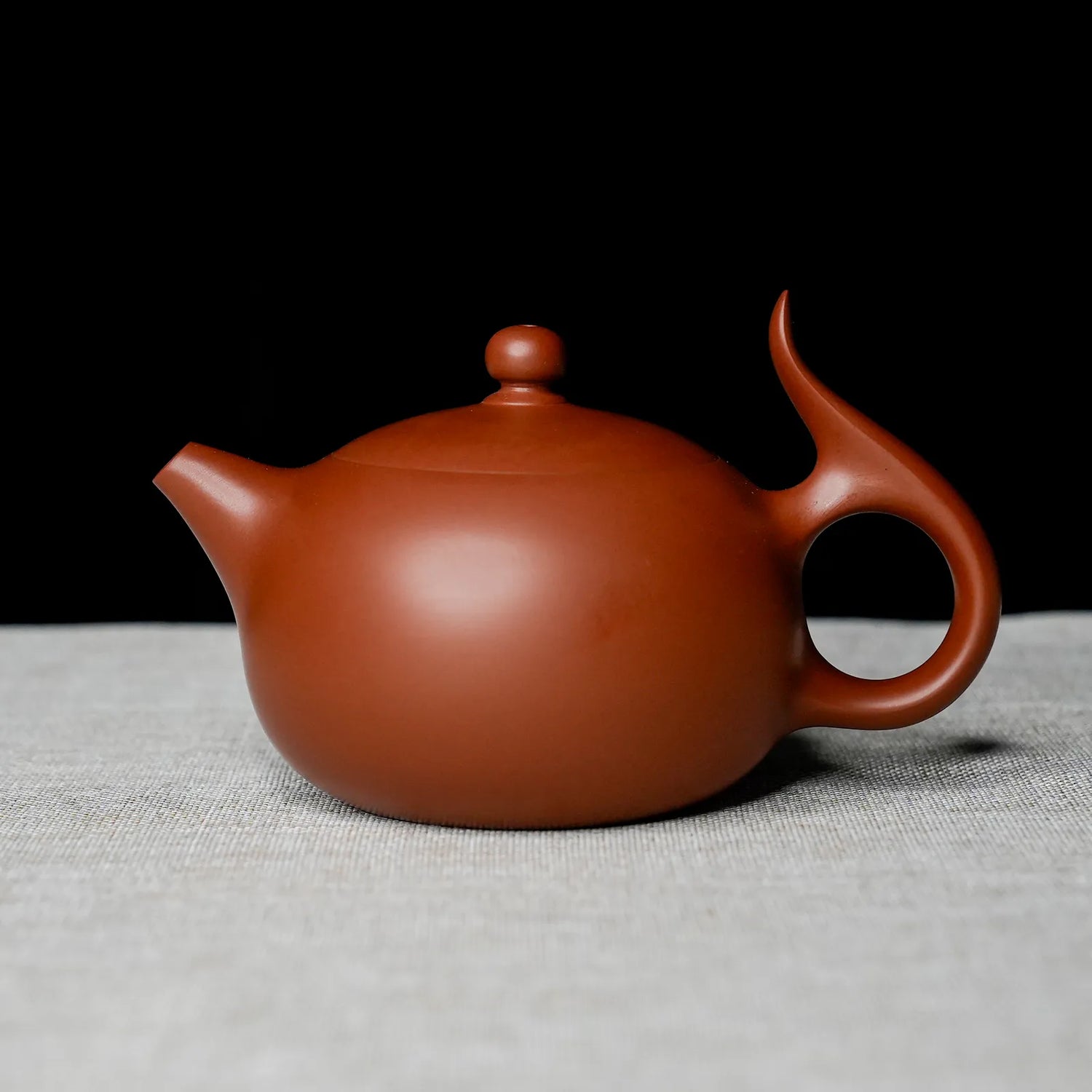 Red clay teapot on a textured surface with a black background