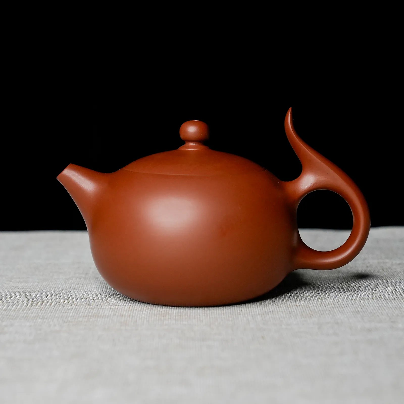 Red clay teapot on a textured surface with a black background